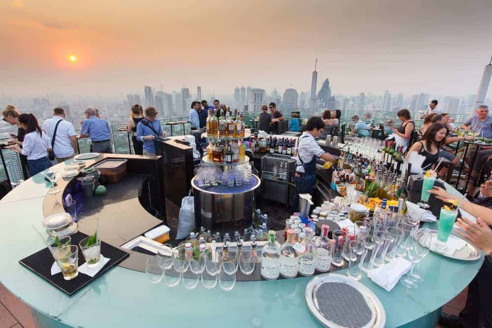 Eine luxuriöse Rooftop Bar mit Kunden, die die Cityline und den Sonnenuntergang genießen.