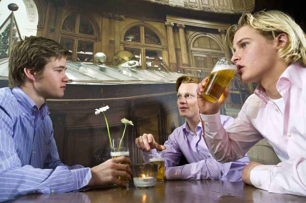 Drei junge Männer mit jeweils einem Glas Bier an einem Tisch in einer Bar.