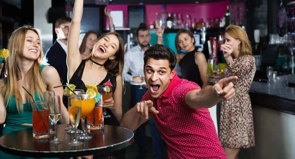  Los amigos de la universidad se divierten en un bar con bebidas en una mesa de bar redonda.