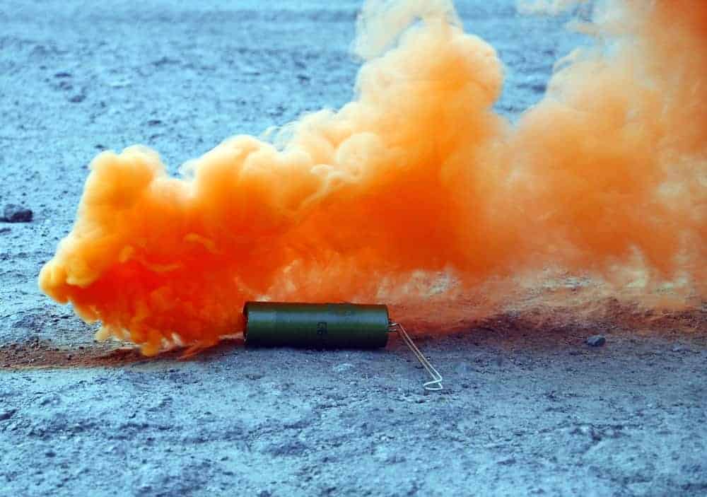 A close look at an orange smoke bomb exploding on the ground.