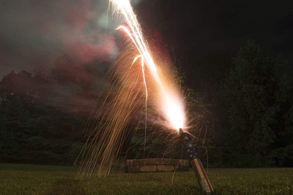 A roman candle with American flag patterns on it shooting off sparks.